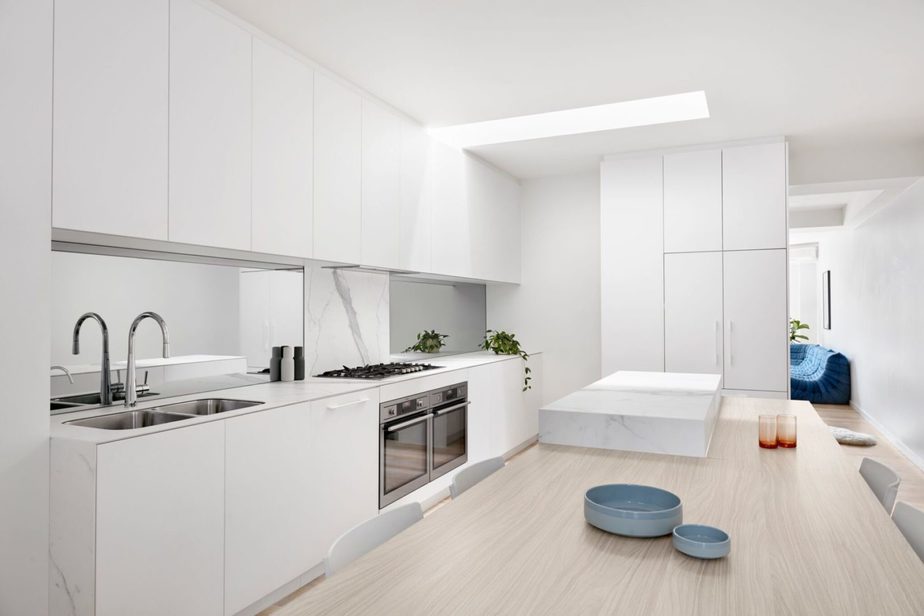 Smarter Bathrooms and Kitchens - a bright modern kitchen with white design, white marbles, and wooden dining. Beautiful kitchen designs built by kitchen renovations Melbourne specialist
