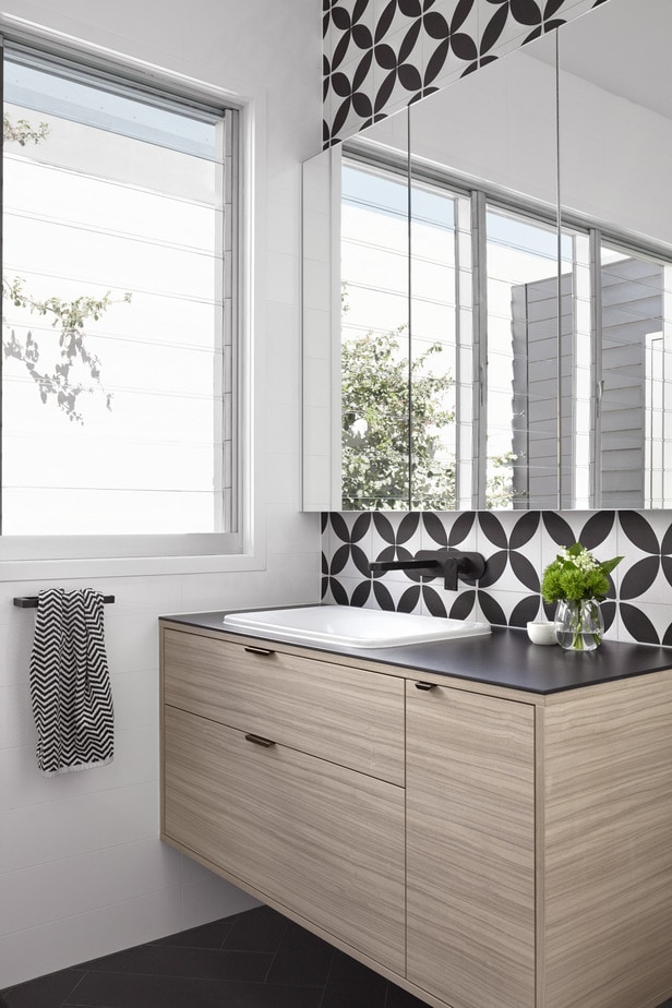 Smarter Bathrooms and Kitchens - a modern bathroom filled with natural lights, stunning wall tiles, large mirror, and ivory white basin. Beautiful bathroom designs built by bathroom renovations specialist Melbourne